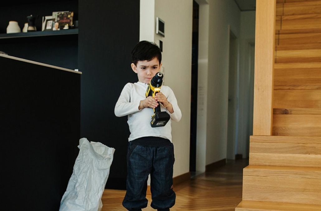 Kind mit Akkuschrauber steht im Wohnzimmer vor den Einzelteilen eines Wurmkiste Selbausets